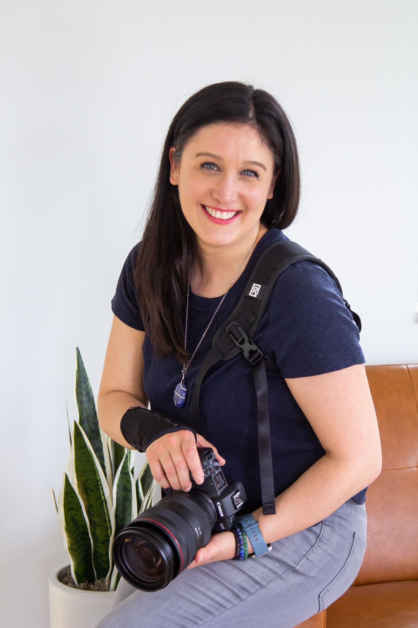 woman lifestyle personal branding photographer holding camera smiling at camera for headshot sitting on couch