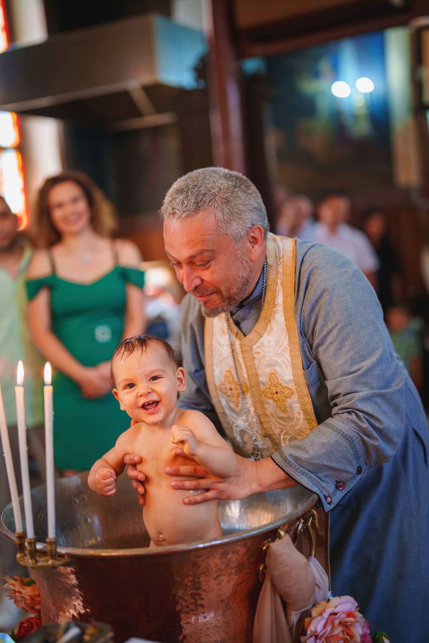 Joyful baptism moment as baby gets held over ceremonial font with candles lit.