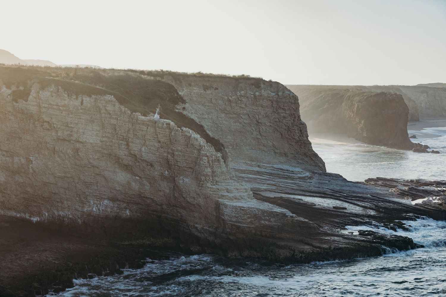 Dramatic coastal cliffs meet the ocean waves during golden hour.