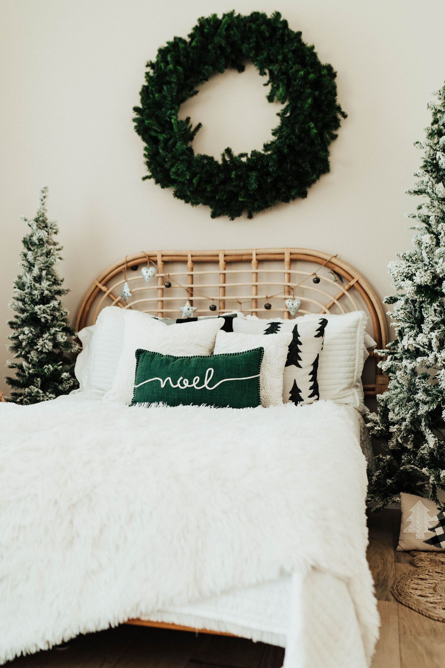 Festive bedroom decor featuring a rattan bed with white bedding, Christmas trees and a green Noel pillow.