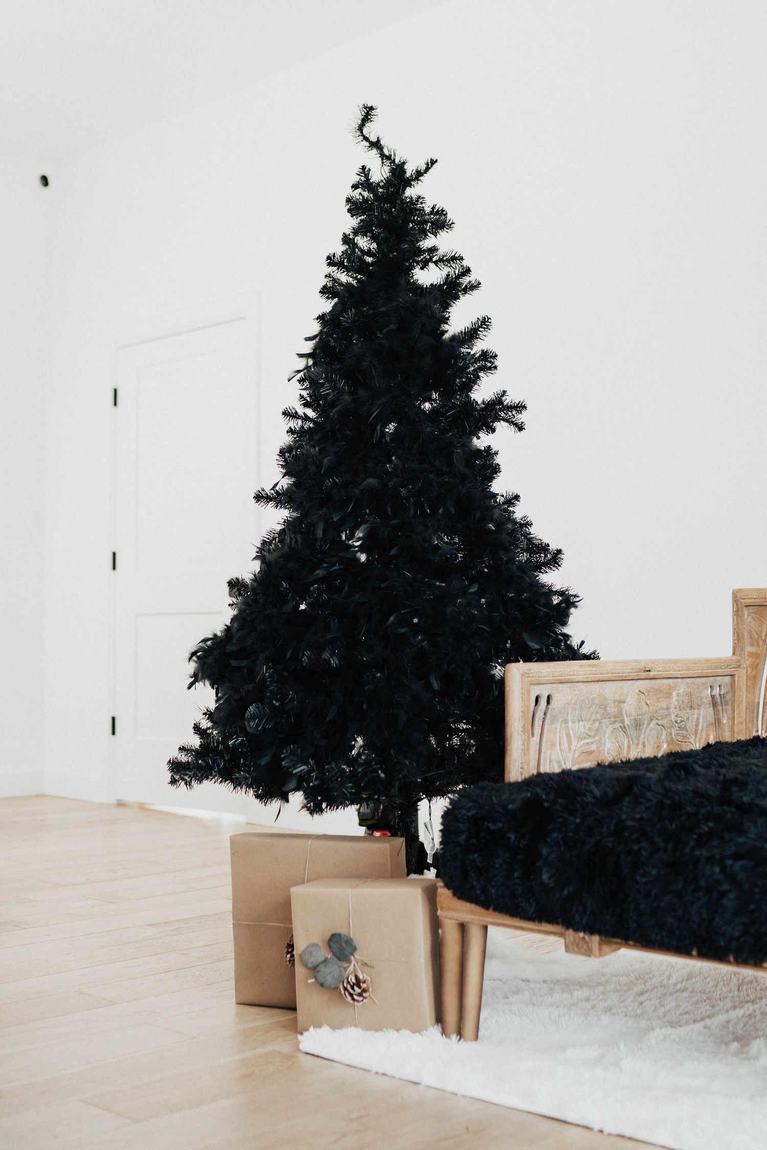 Black Christmas tree with wrapped presents underneath on light wooden flooring.