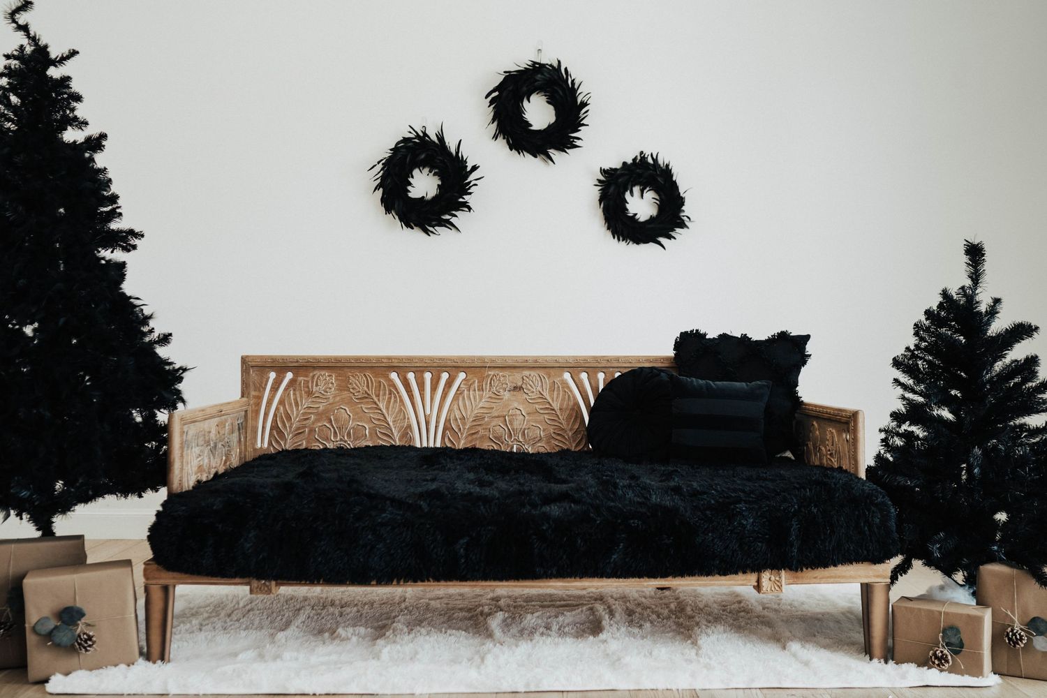 Modern black and wood bench with three dark wreaths on white wall and Christmas trees.