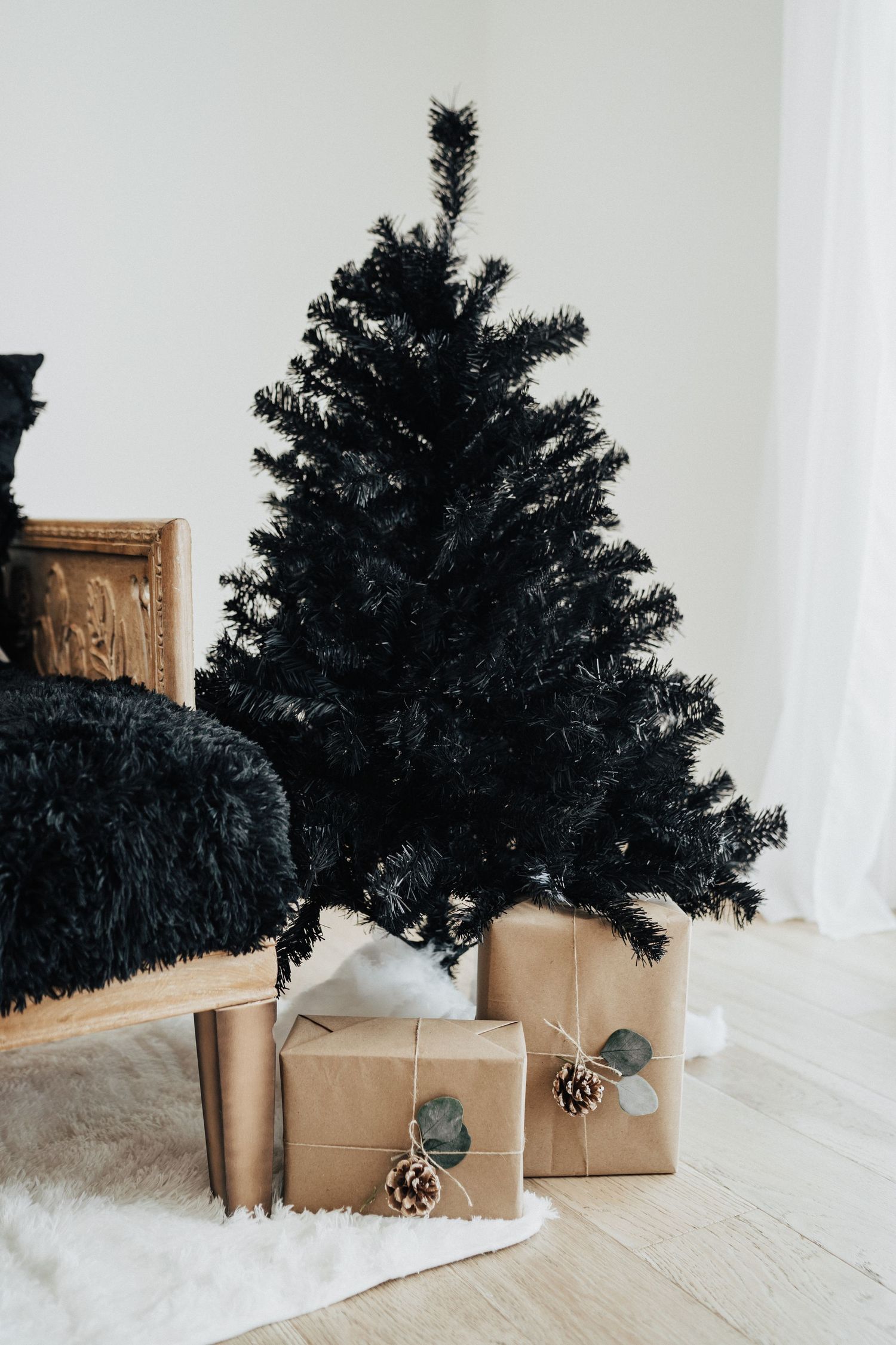 Black artificial Christmas tree with brown paper wrapped gifts decorated with pinecones.