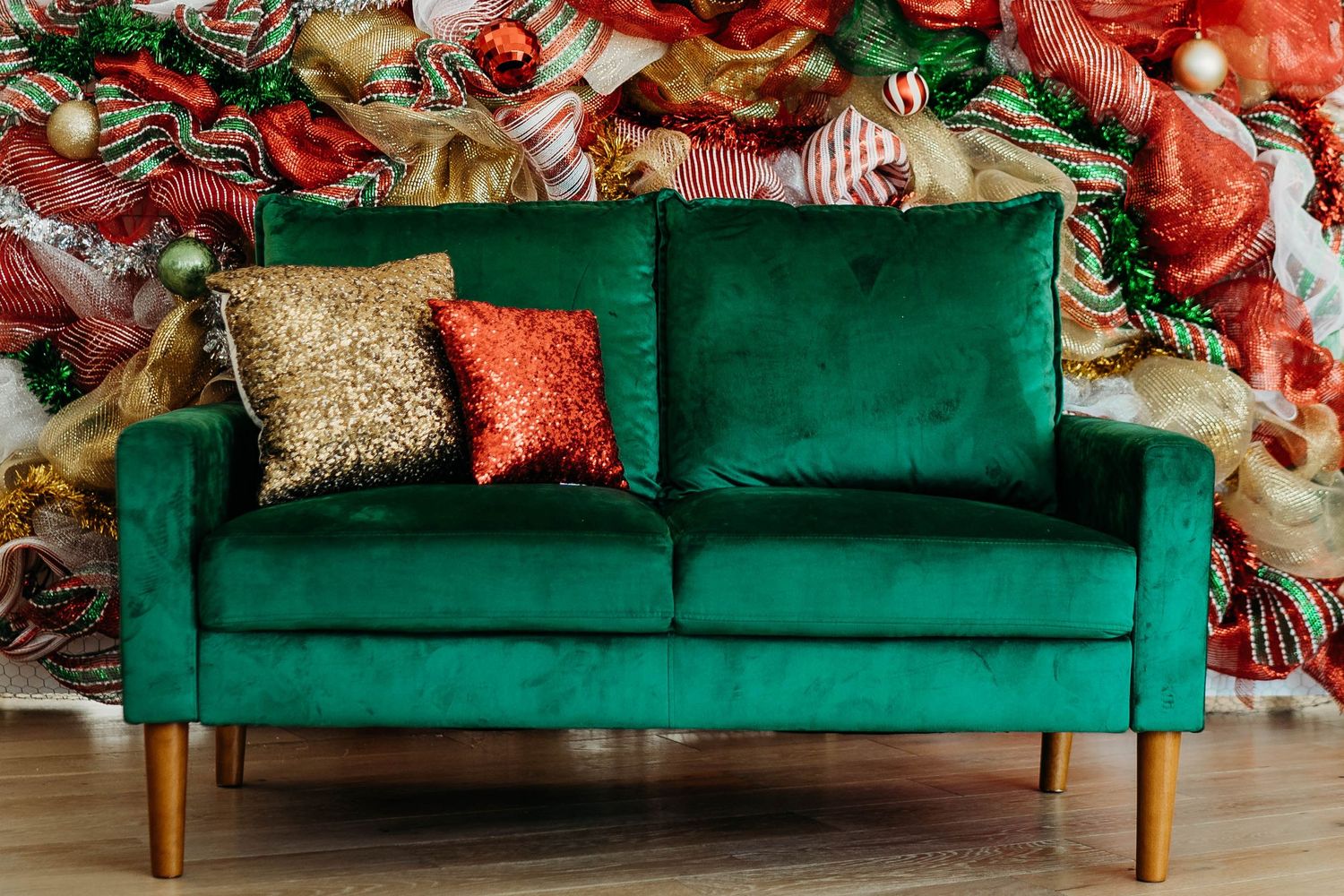 Modern emerald velvet sofa with gold and red throw pillows against a festive red and white wall display.