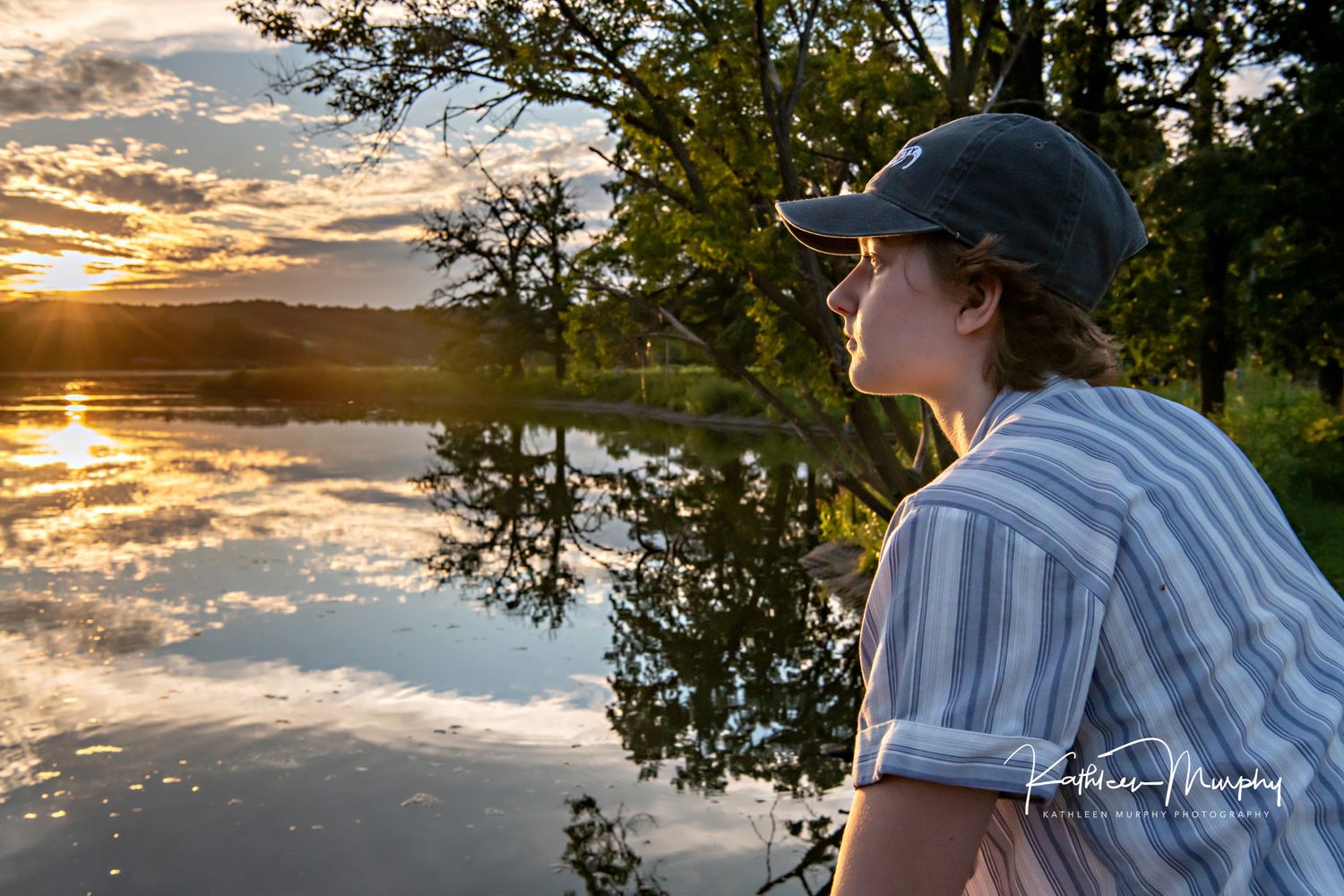 A silhouette watching a stunning sunset over a tranquil lake with trees reflected in the golden water.