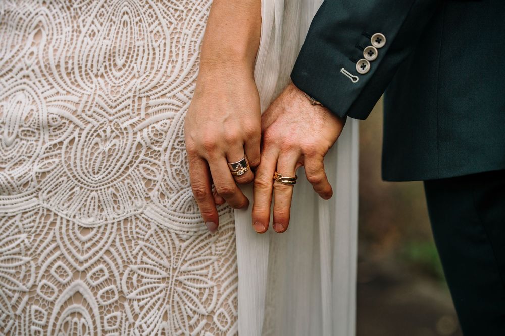 Close-up of hands showing wedding rings against a white lace dress backdrop.