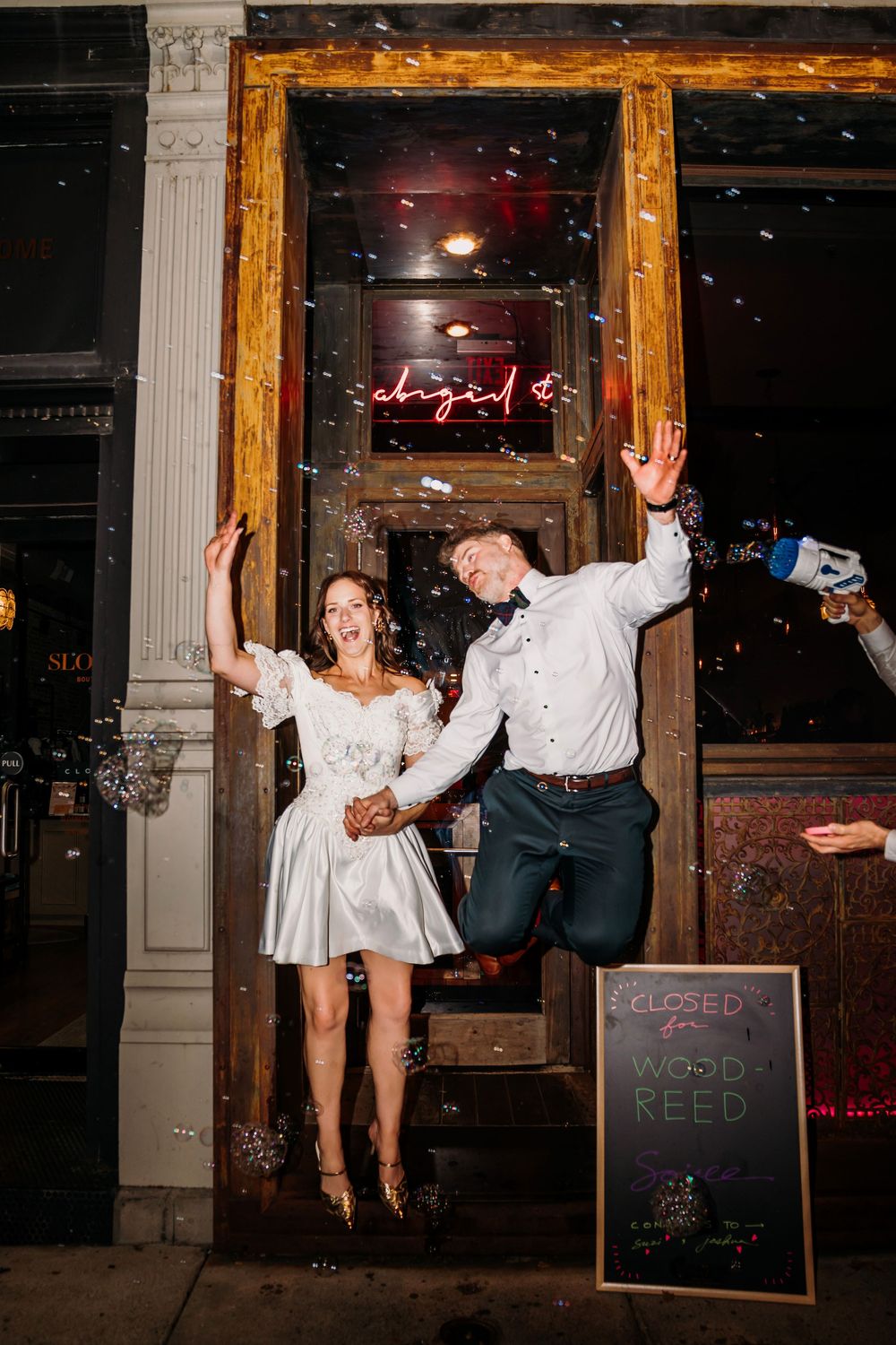 Fun sequence of wedding guests jumping and dancing in front of an illuminated storefront at night.