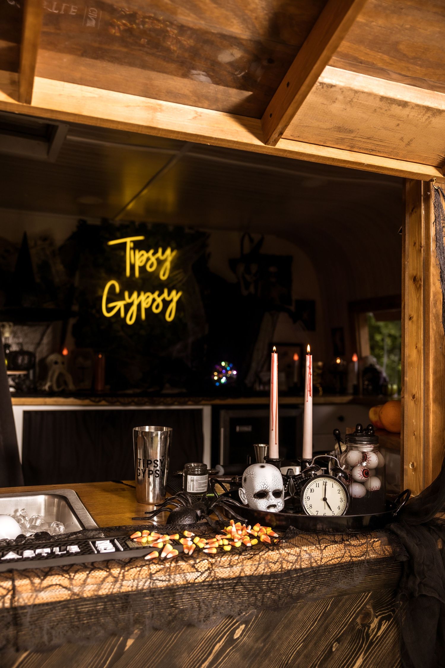Neon 'Tipsy Gypsy' sign illuminates a dark bar counter with Halloween decorations.