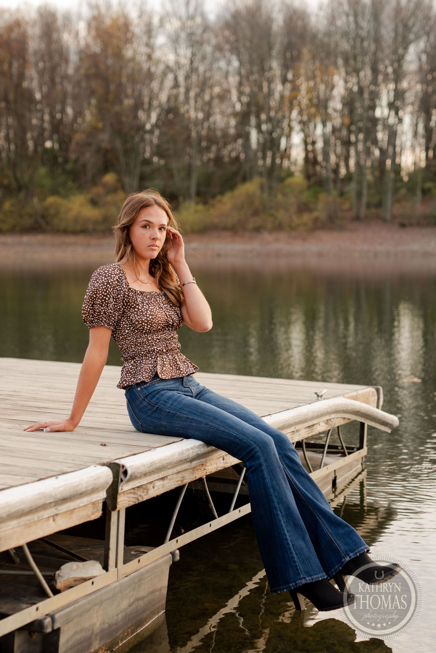 A leopard print top and flare jeans outfit photographed on a wooden dock by a serene lake at sunset.