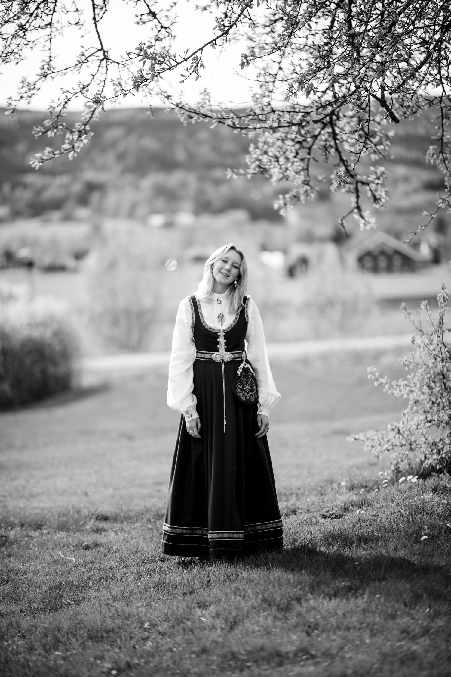 Black and white photo of traditional Nordic folk costume in pastoral landscape with spring blossoms.