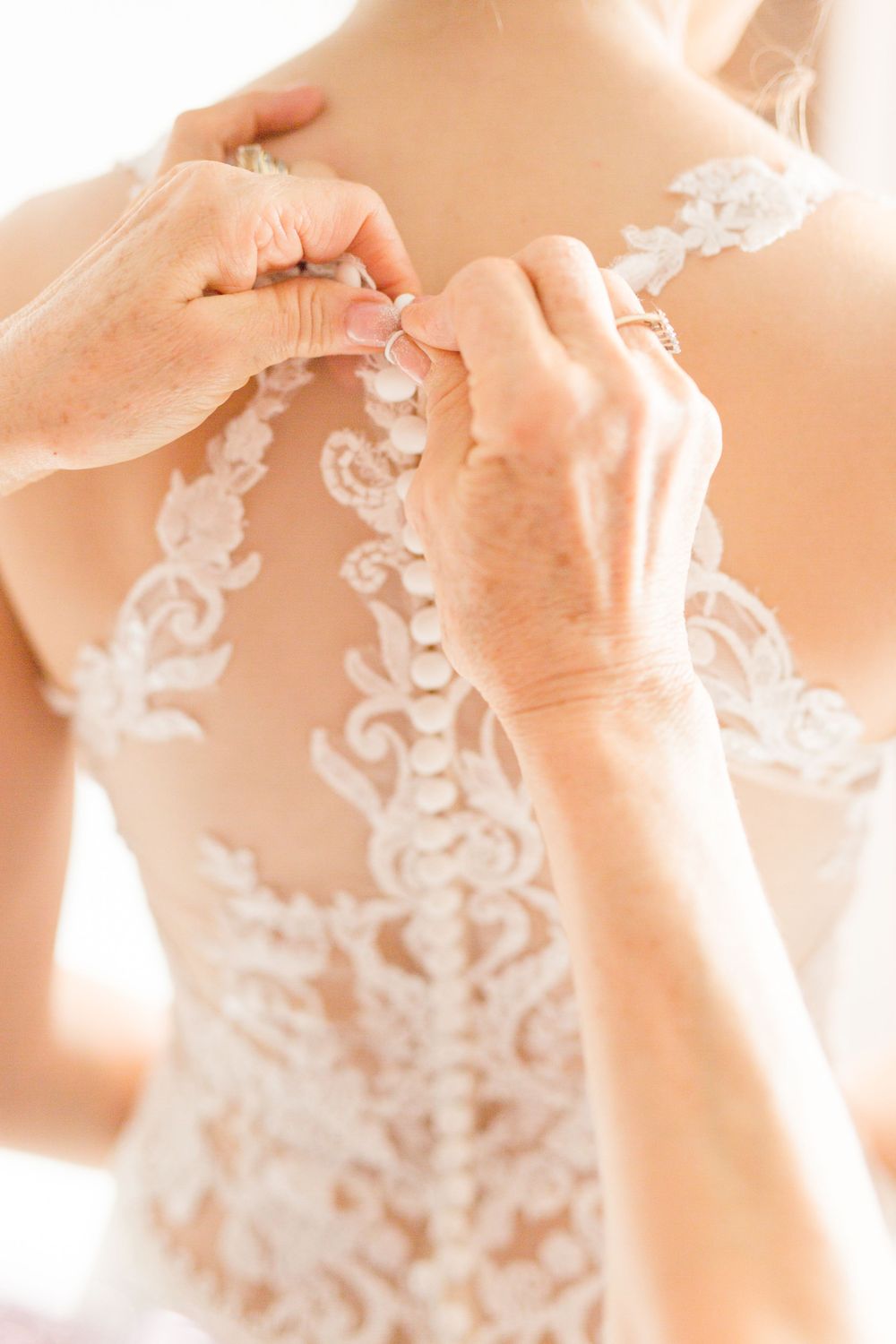 Close-up detail of intricate lace pattern being fastened on back of wedding dress.