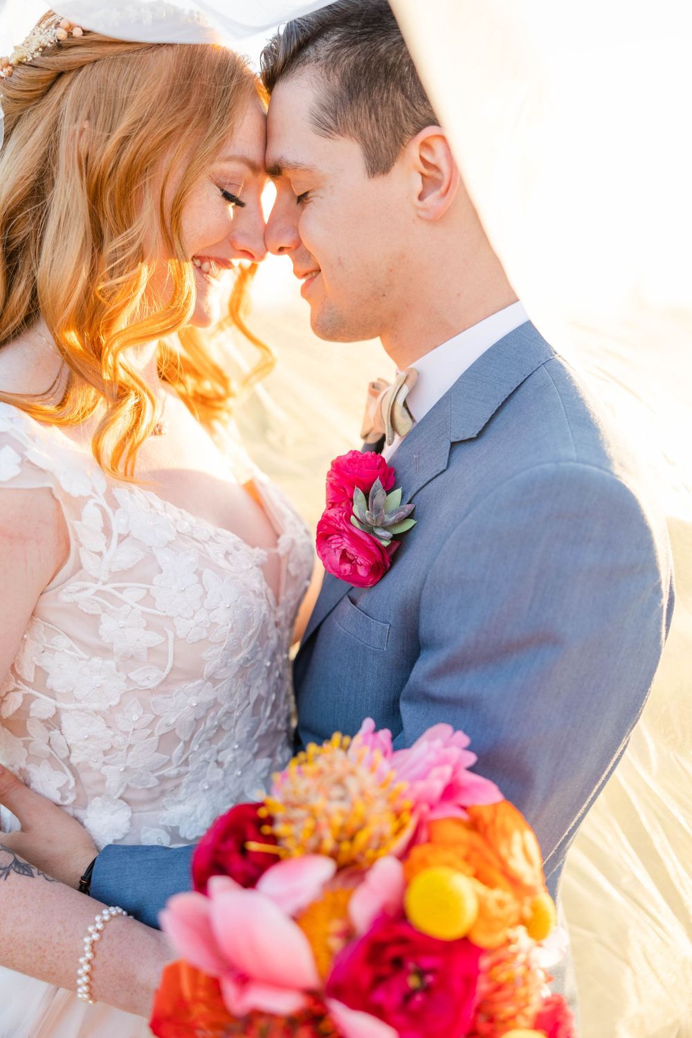 Romantic wedding portrait with vibrant pink floral bouquet against soft sunset lighting.