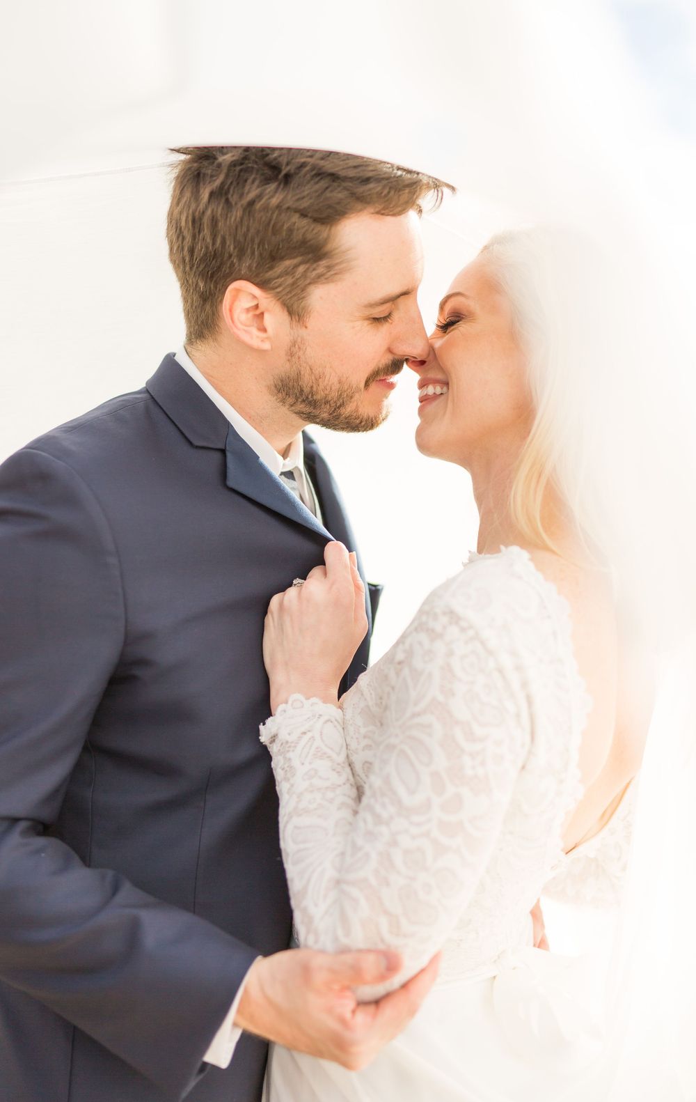 A romantic moment between newlyweds with the bride in white lace and groom in navy suit embracing.