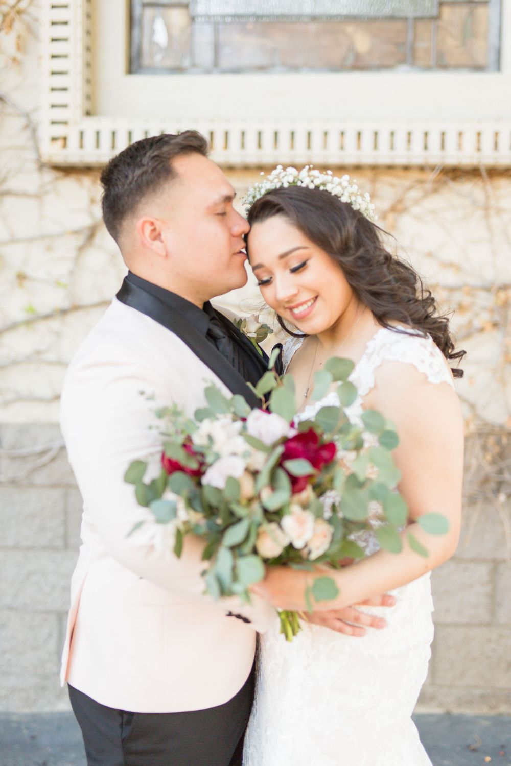 Wedding couple sharing intimate moment with bouquet of red and white flowers.