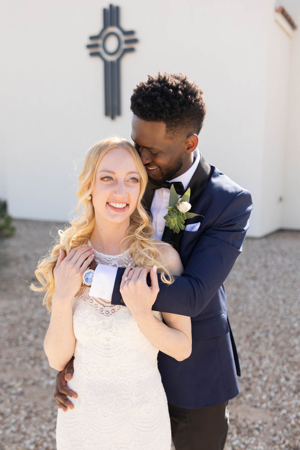 Wedding couple posing together with decorative cross symbol in background.