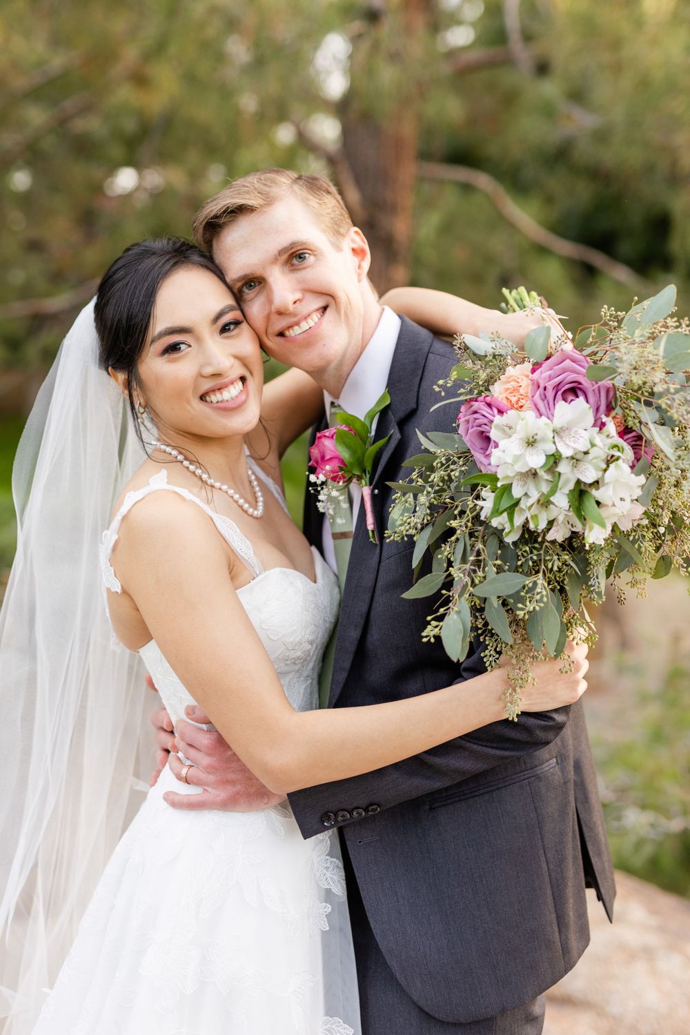 A happy couple embraces while holding a stunning pink and white floral bouquet on their wedding day.