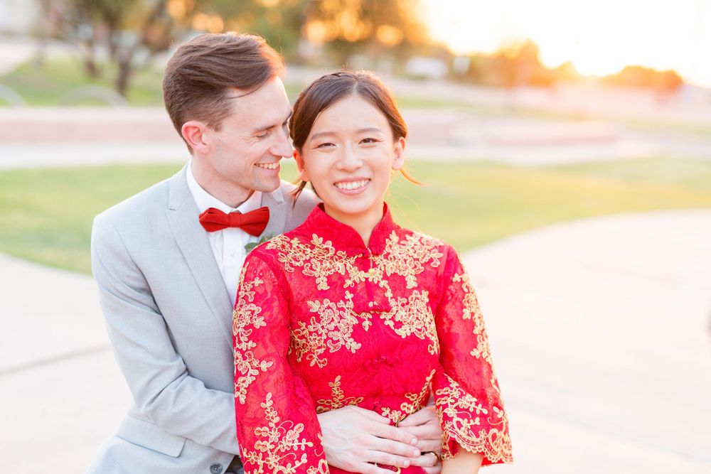A couple in wedding attire embracing at sunset, with bride in traditional red Chinese dress.