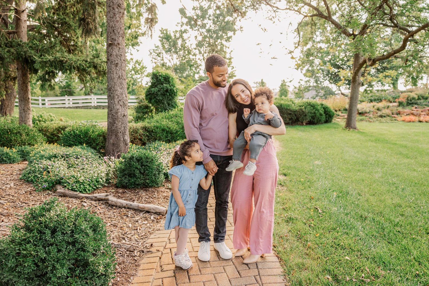 A family of three standing together on a brick pathway in a lush garden setting.