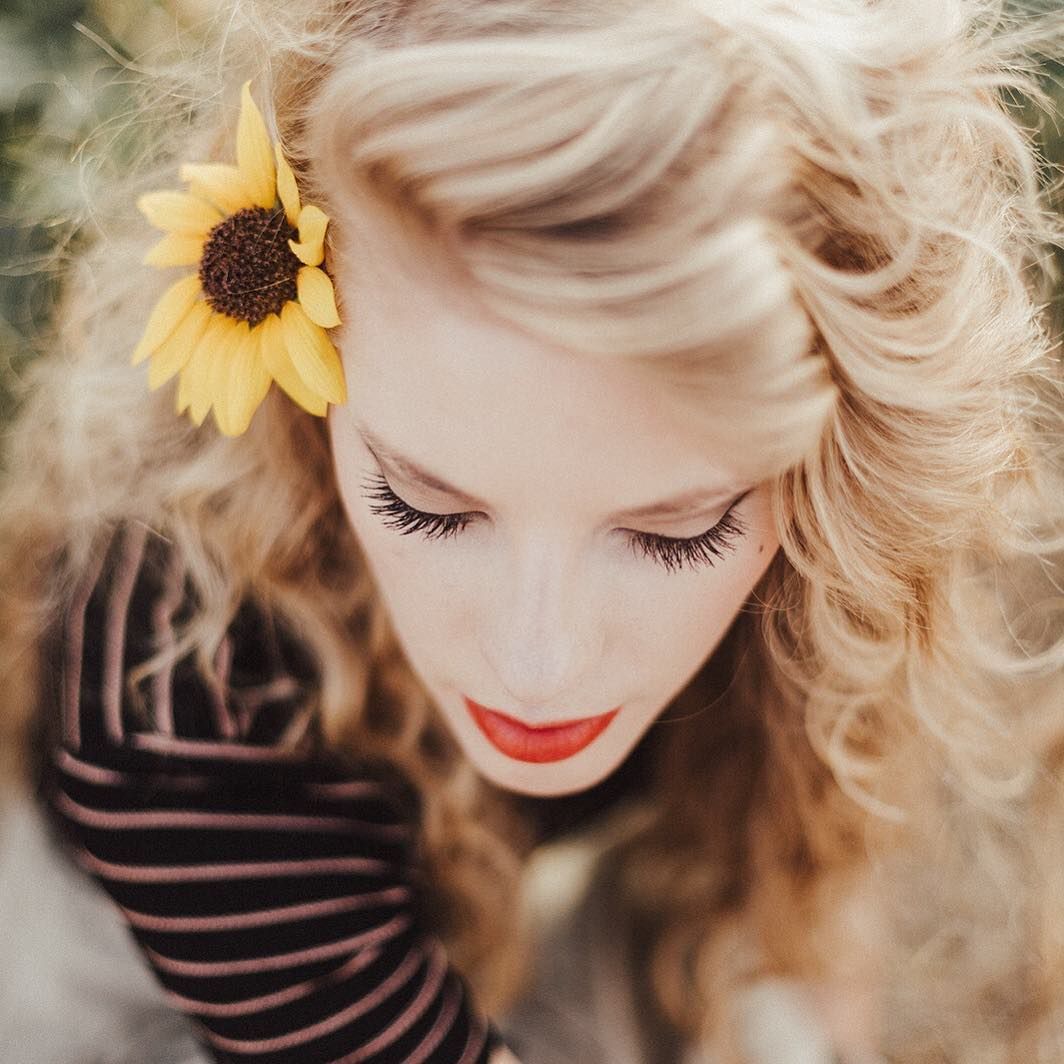 Close-up portrait of blonde hair with sunflower accent and red lipstick.
