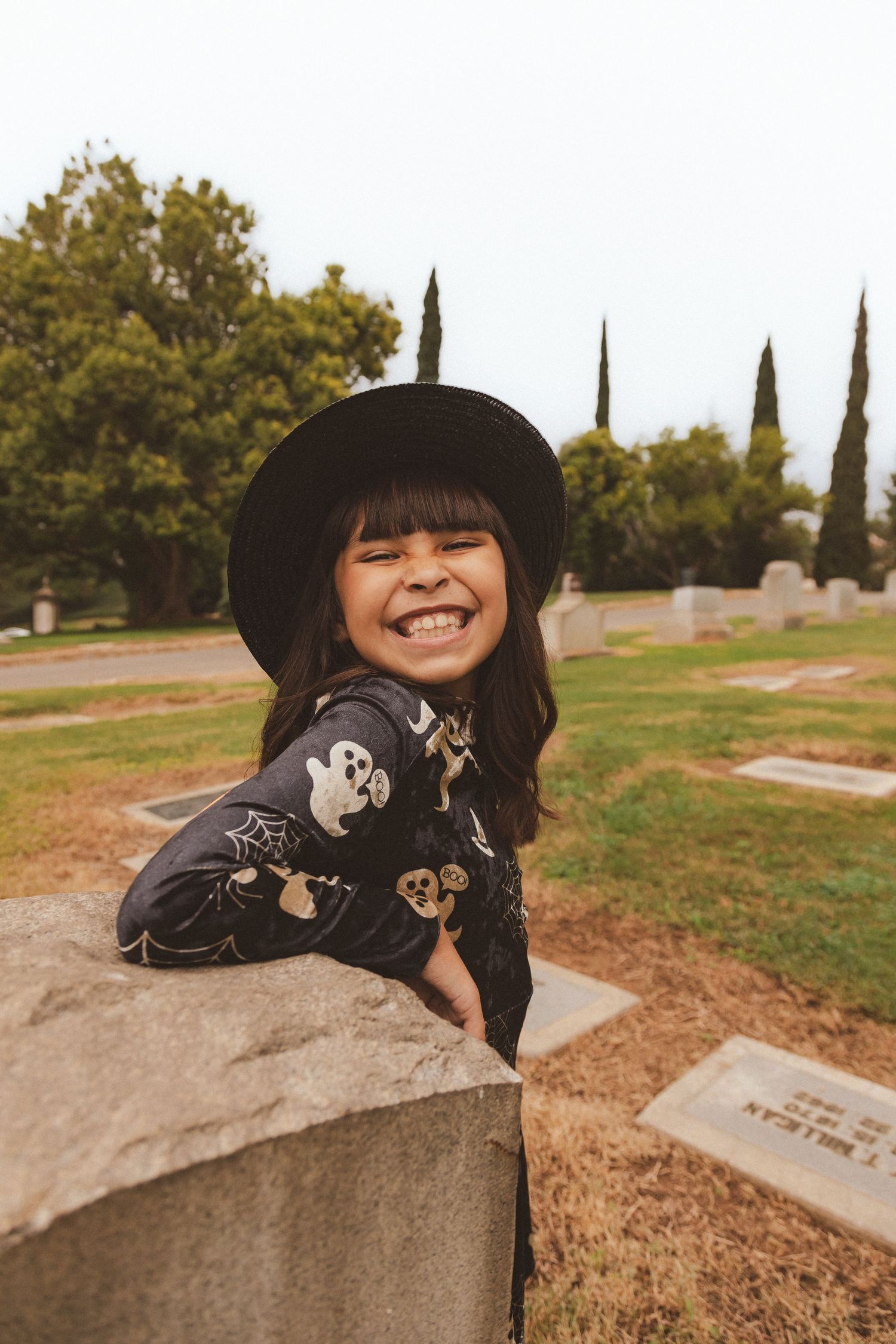A person in a black hat smiling while posing near gravestones in a cemetery.