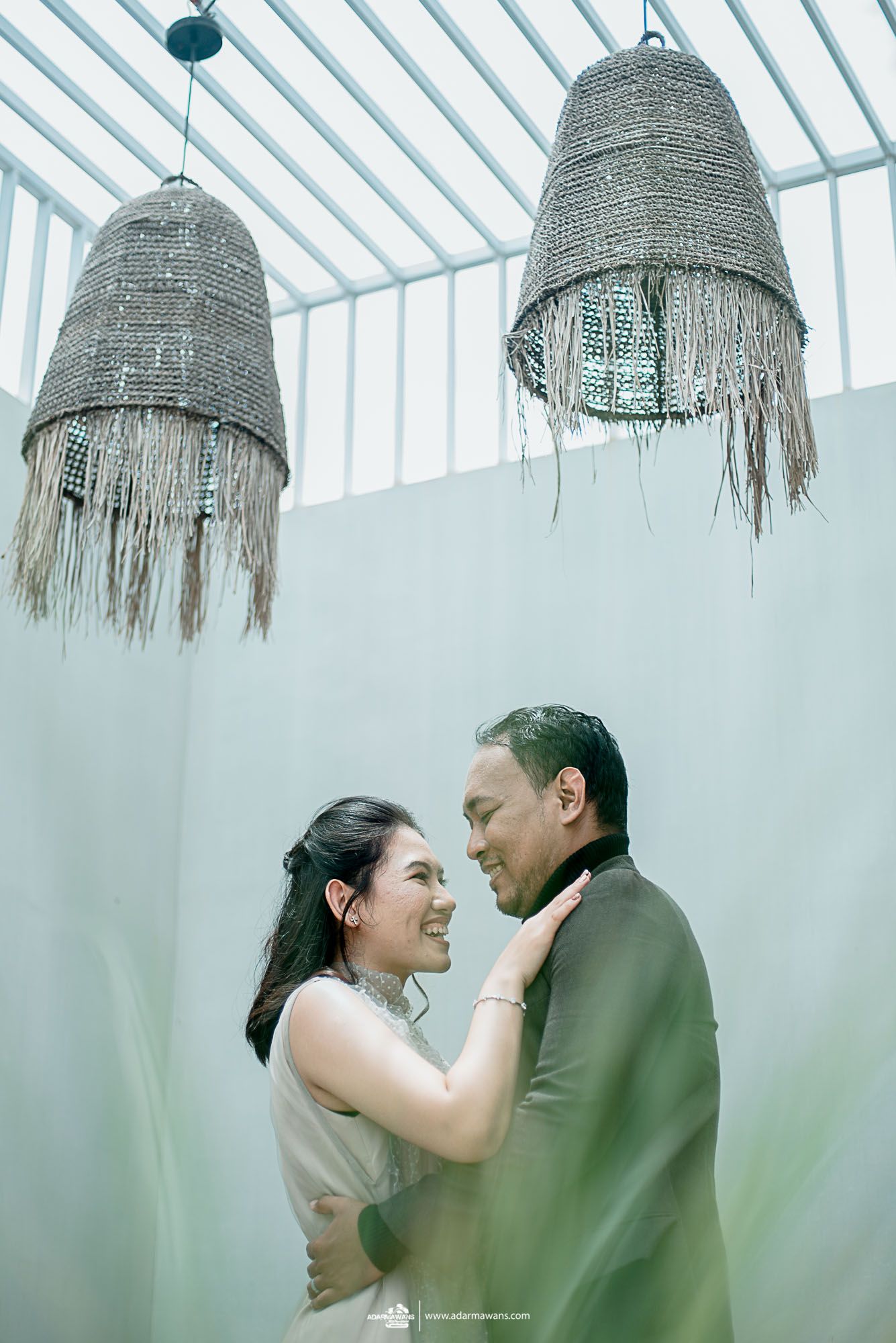 A couple embraces under large woven pendant lights in an indoor setting.