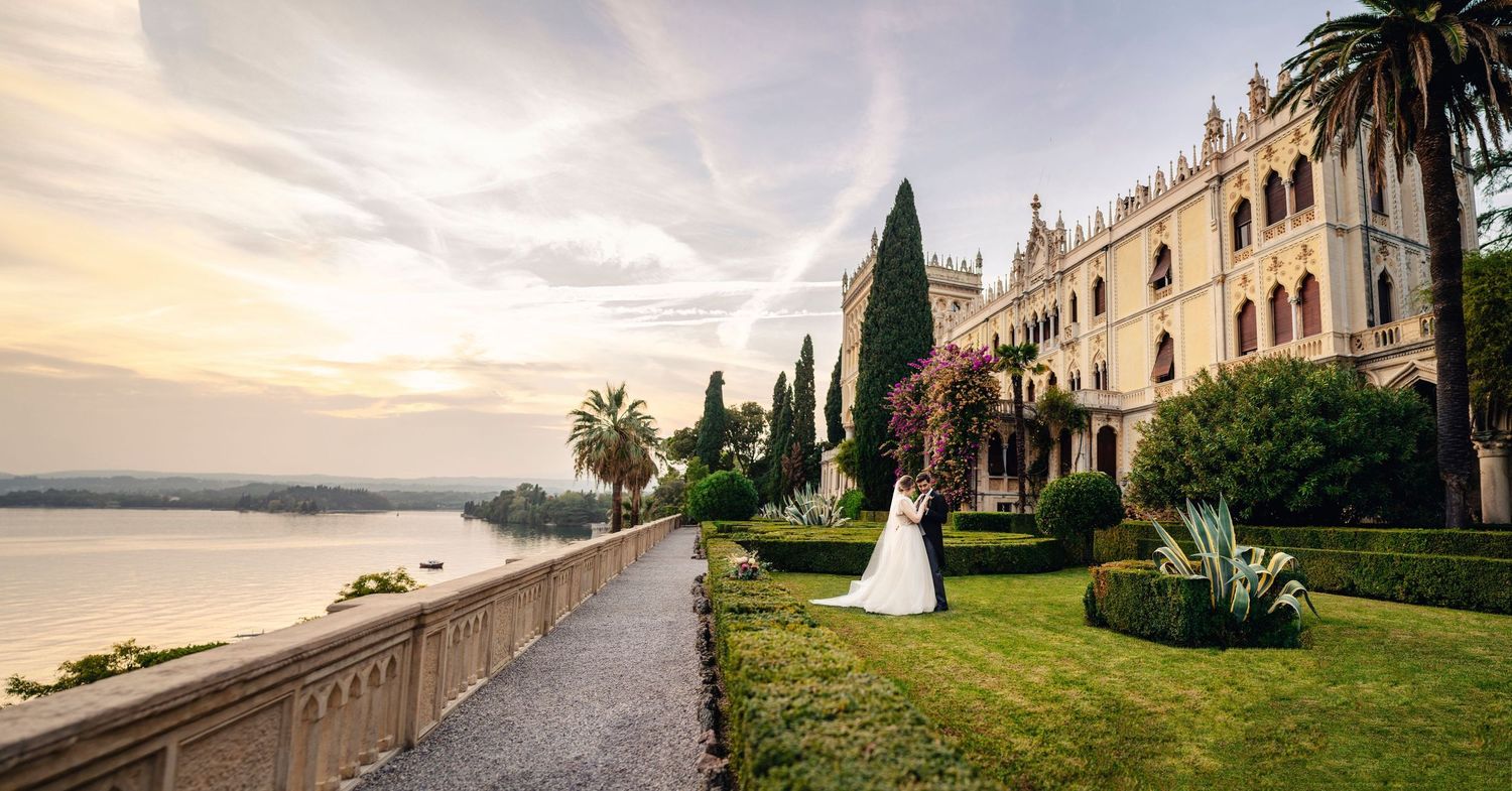 Panoramic view of a grand Mediterranean villa with palm trees and waterfront during golden sunset.