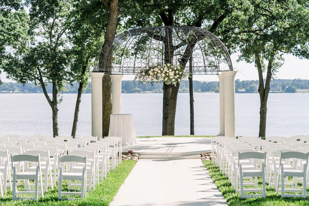 Waterfront wedding ceremony setup with white chairs and archway framed by trees.