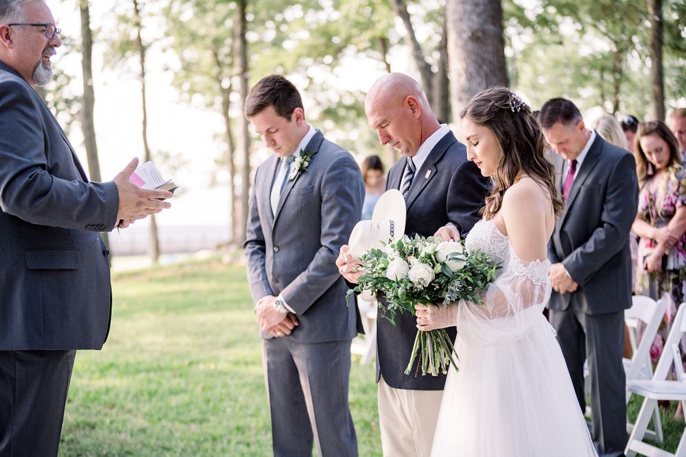 Outdoor wedding ceremony in progress with guests seated on white chairs.