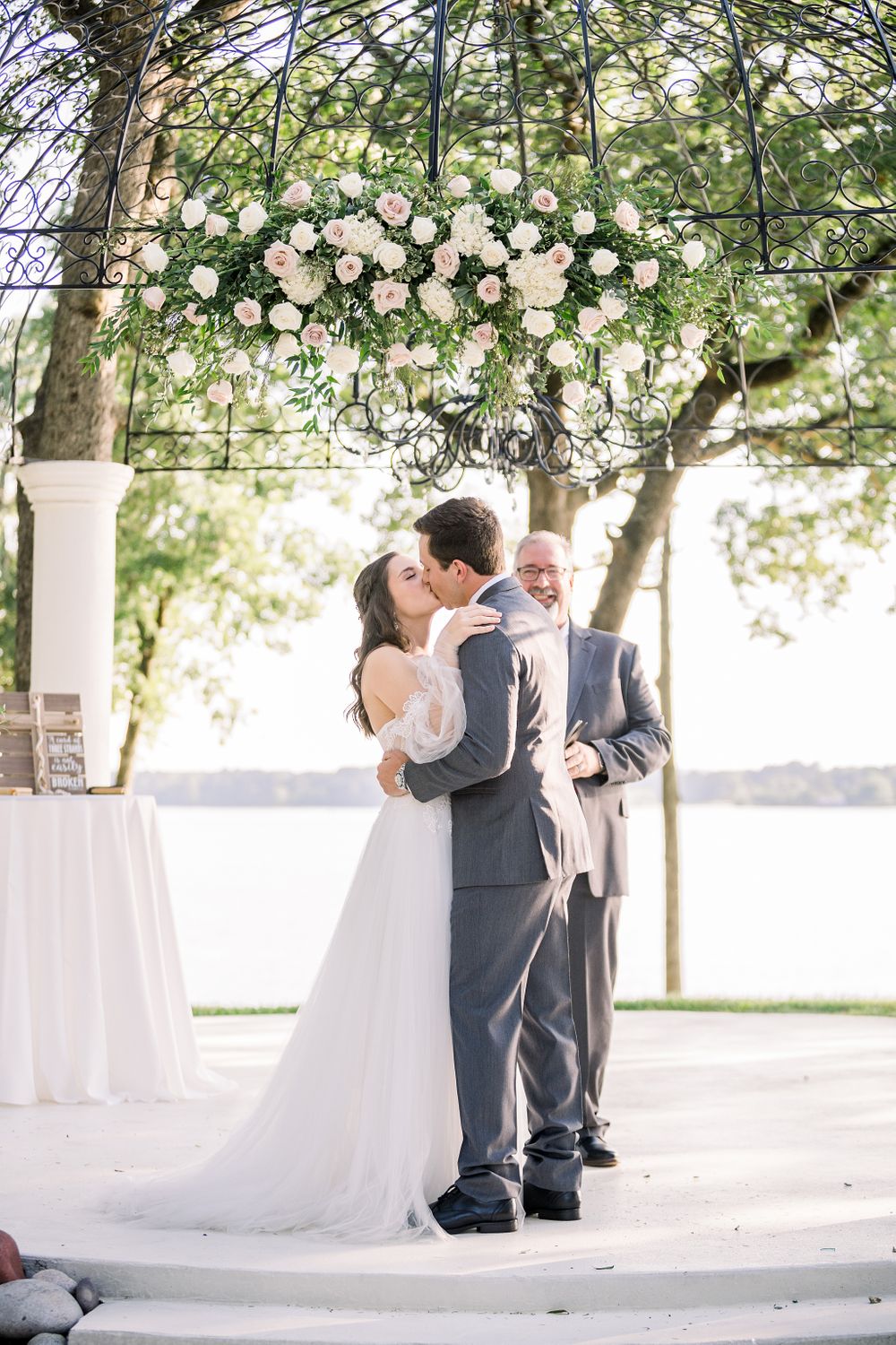 Romantic outdoor wedding ceremony under a floral chandelier with white roses and greenery.