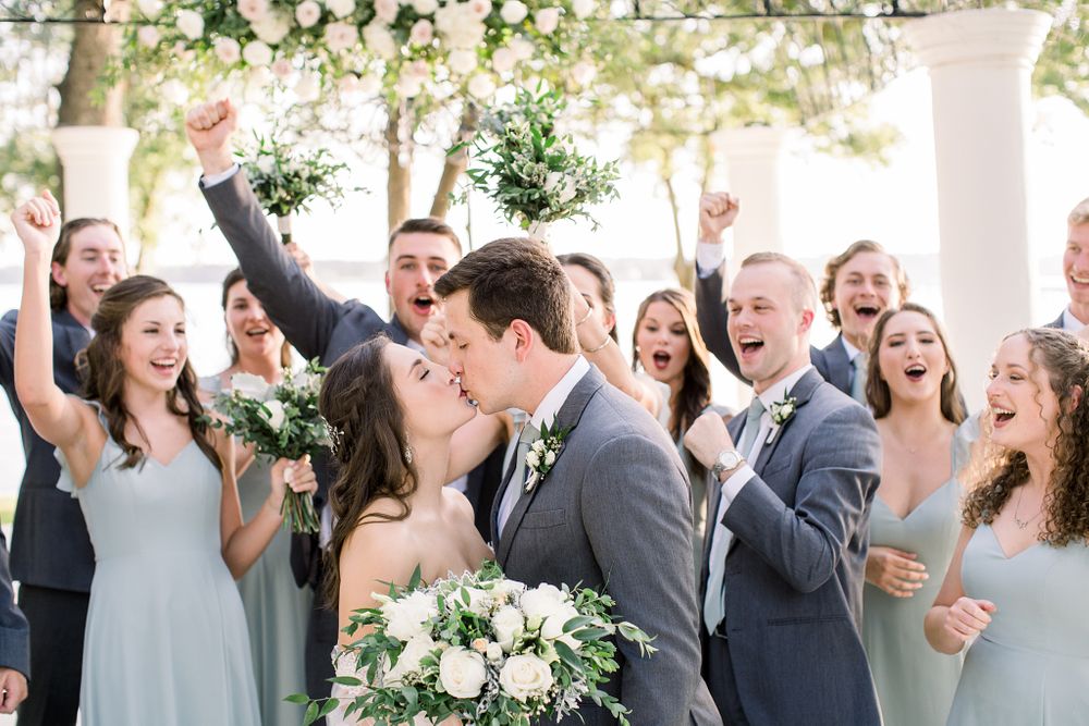 Wedding party and guests celebrate joyfully under a floral-decorated outdoor pavilion.