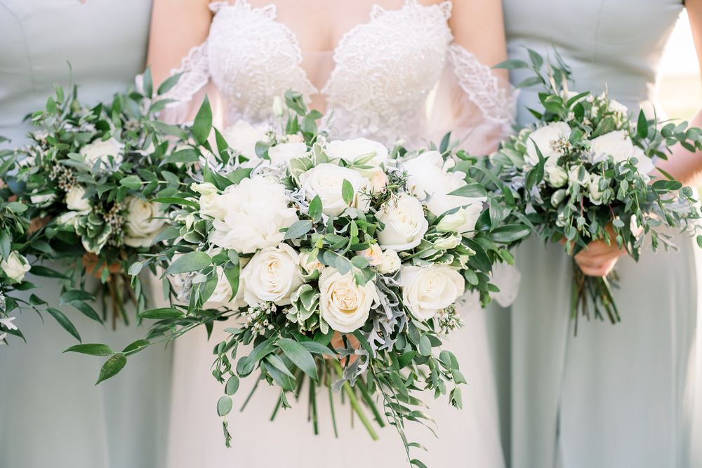 Elegant white rose and greenery bouquets held against sage bridesmaid dresses.