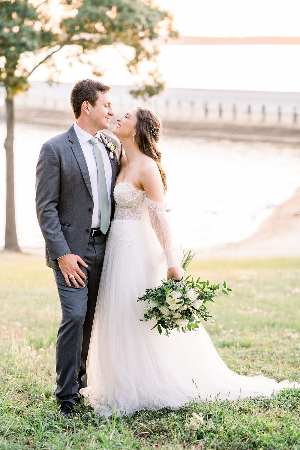A romantic outdoor wedding portrait with a waterfront backdrop during golden hour.