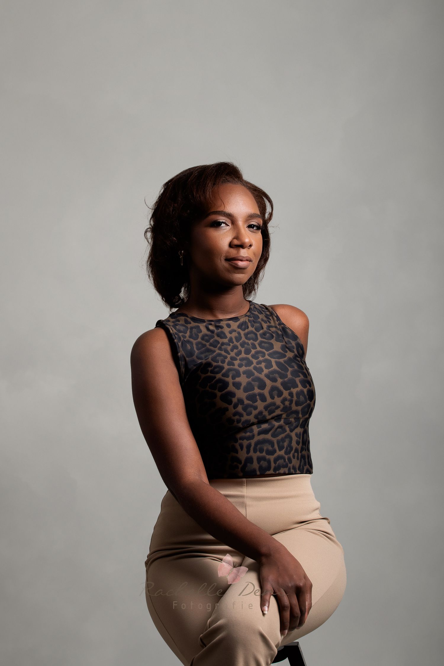 Professional studio portrait of a model wearing a leopard print crop top and beige pants against a gray backdrop.