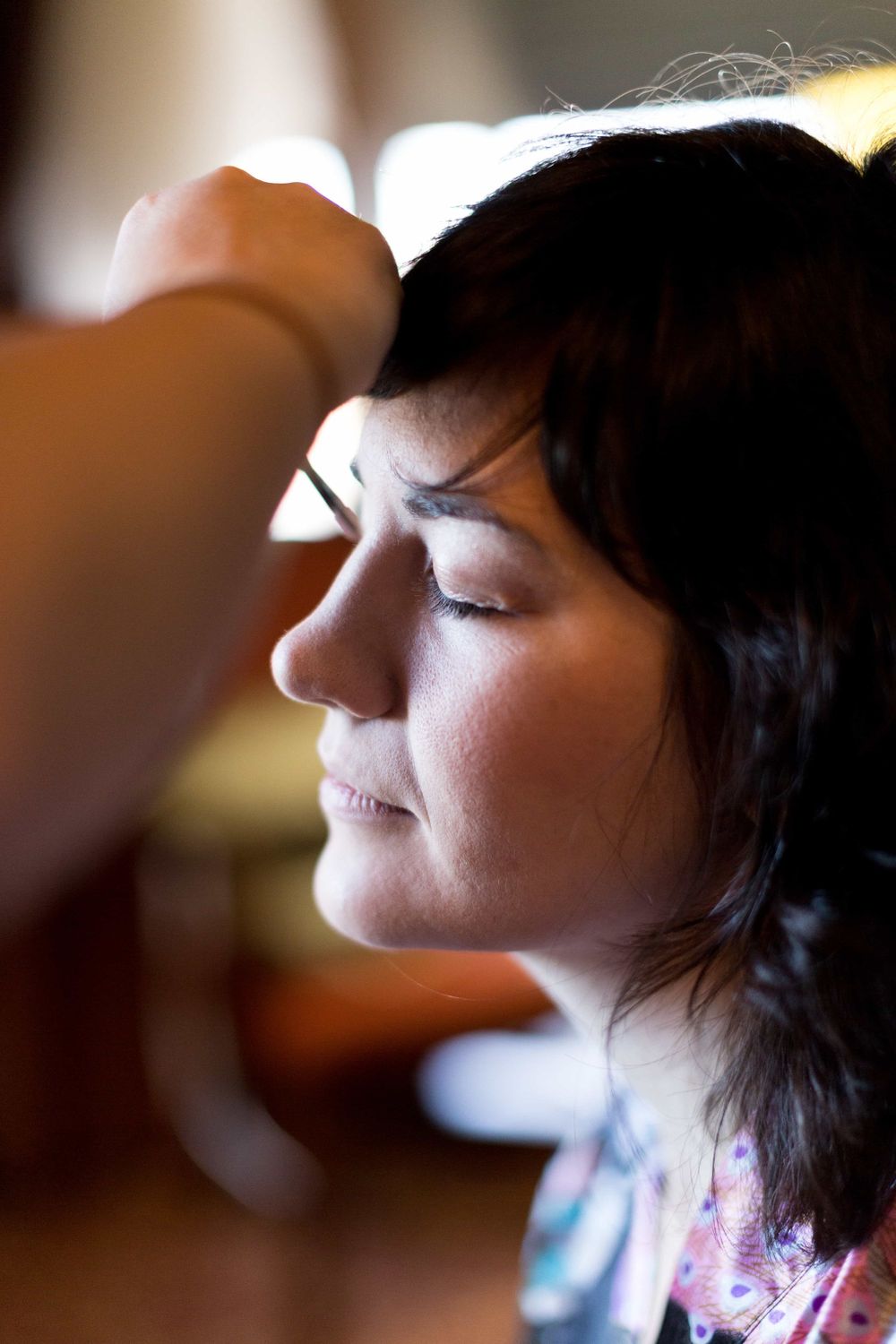 Dark-haired bride with eyes closed getting makeup applied before her wedding ceremony.