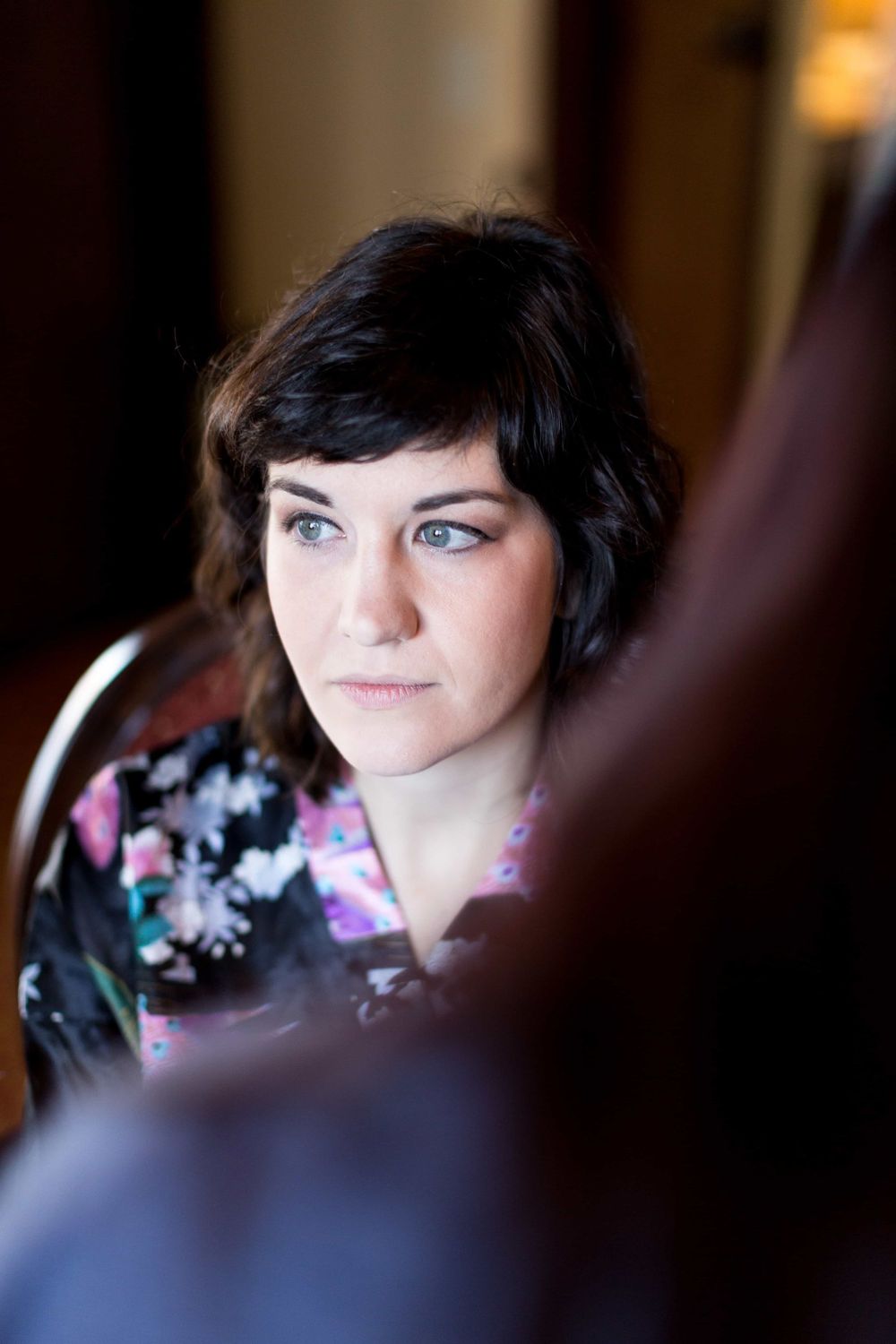 Beautiful blue-eyed bride in floral robe with short dark hair gazing forward before wedding.