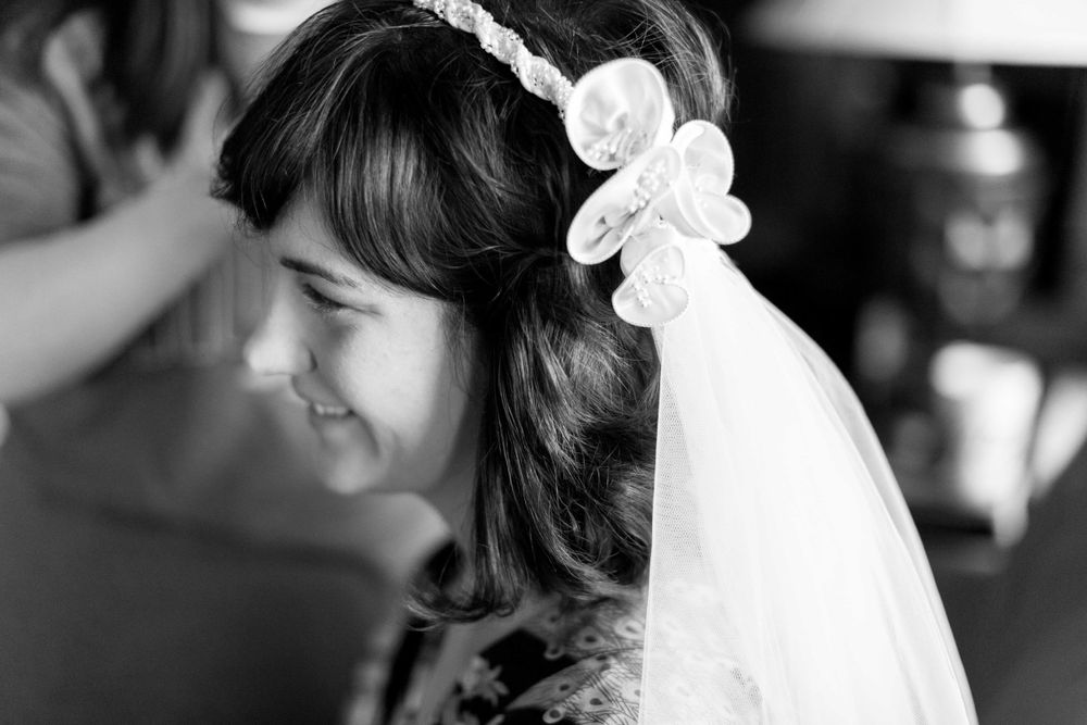 Black and white portrait of smiling bride with floral headband and flowing veil.