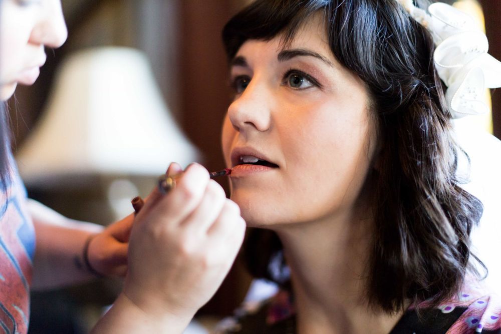 Close-up of dark-haired bride having makeup applied with floral hair accessory visible.