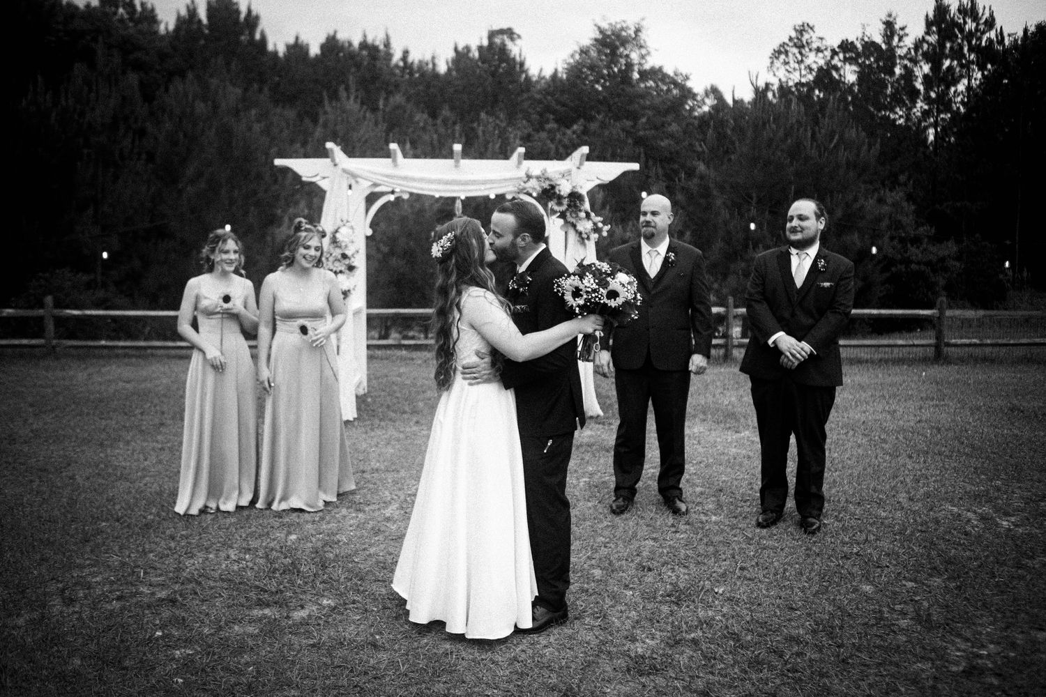 Wedding ceremony taking place under an outdoor arbor in black and white.
