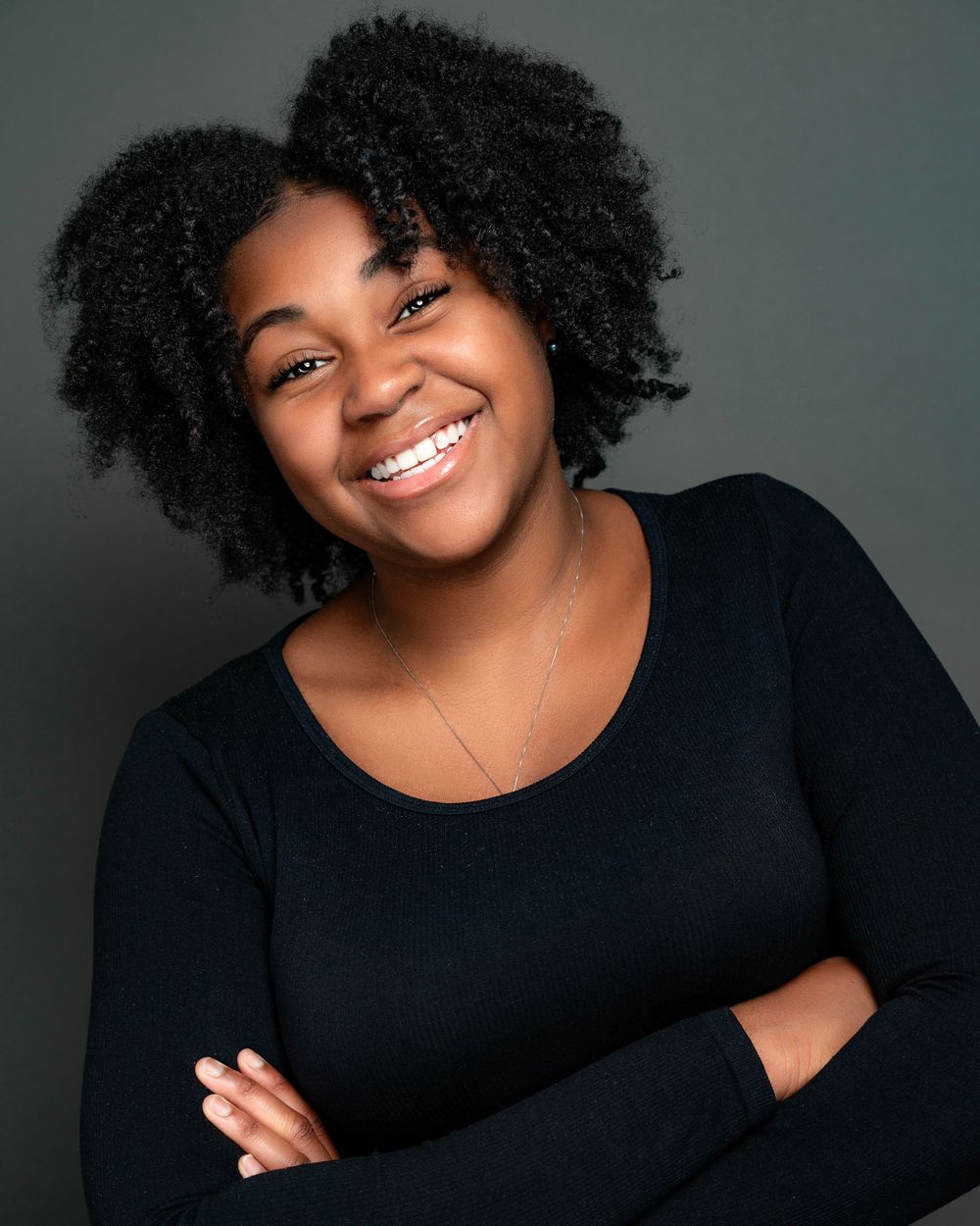 Studio portrait with natural curly hair and black top against gray background.