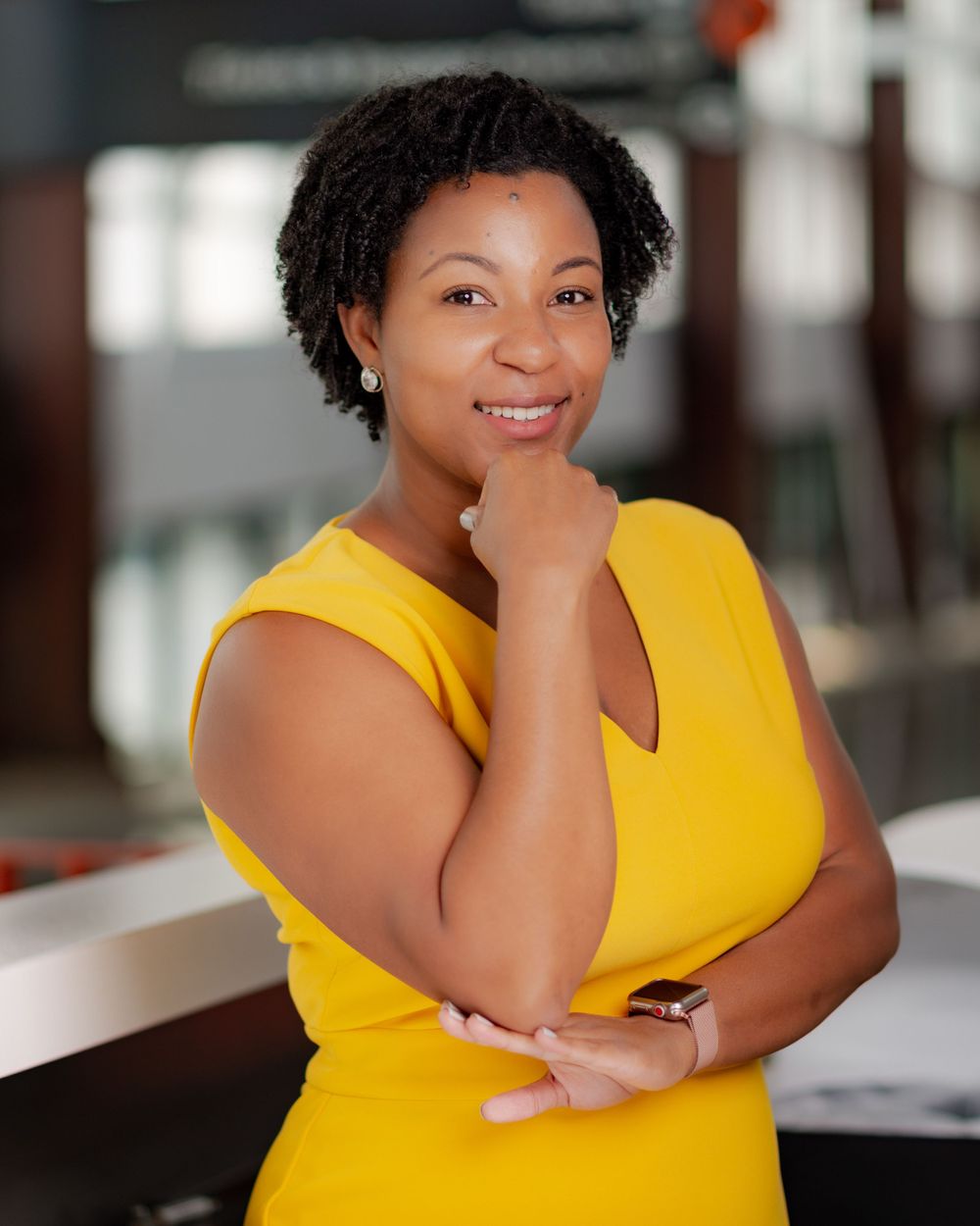 Professional headshot in bright yellow sleeveless top with hand posed thoughtfully.