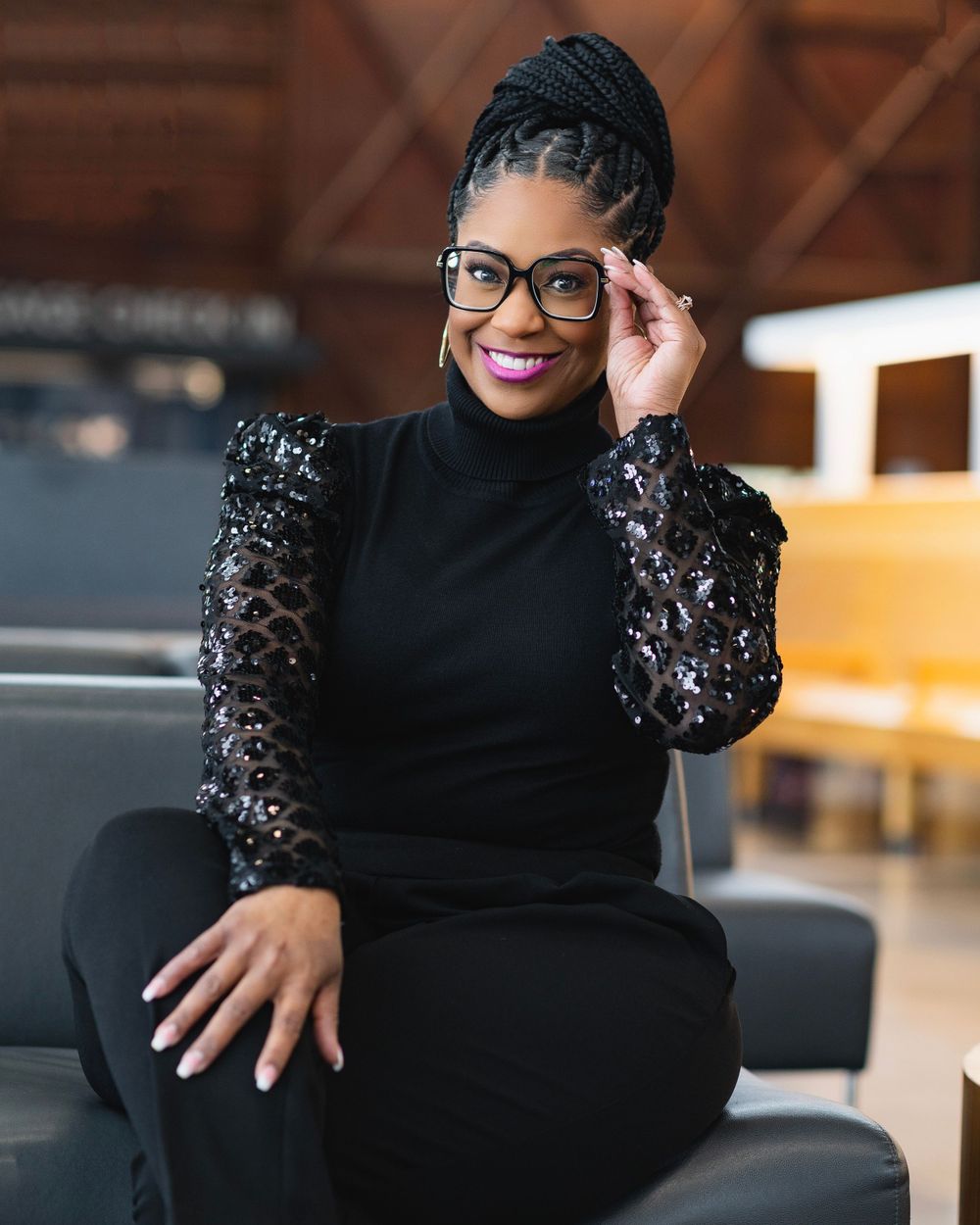 Professional portrait in black lace sleeve top and glasses seated in modern office setting.
