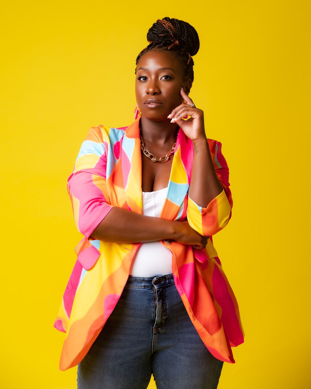 A vibrant colorful blazer worn with jeans and a white top against a bright yellow background.