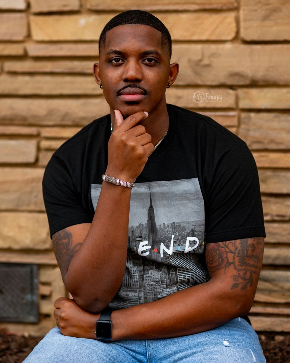 Portrait against stone wall wearing black t-shirt with cityscape graphic.