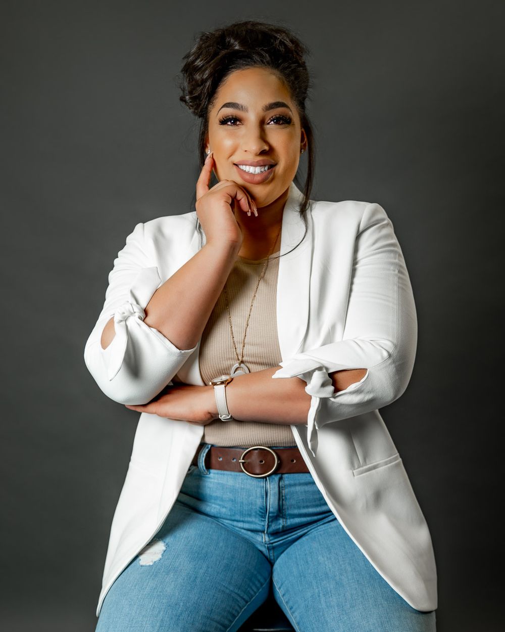 Professional portrait in white blazer and jeans against dark grey background.