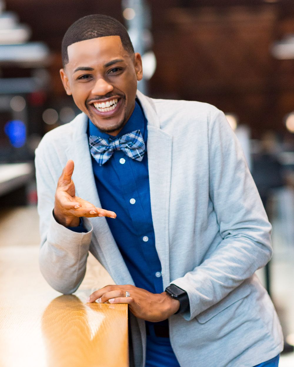 Professional wearing a light blue blazer, navy shirt and bow tie gestures while smiling warmly.