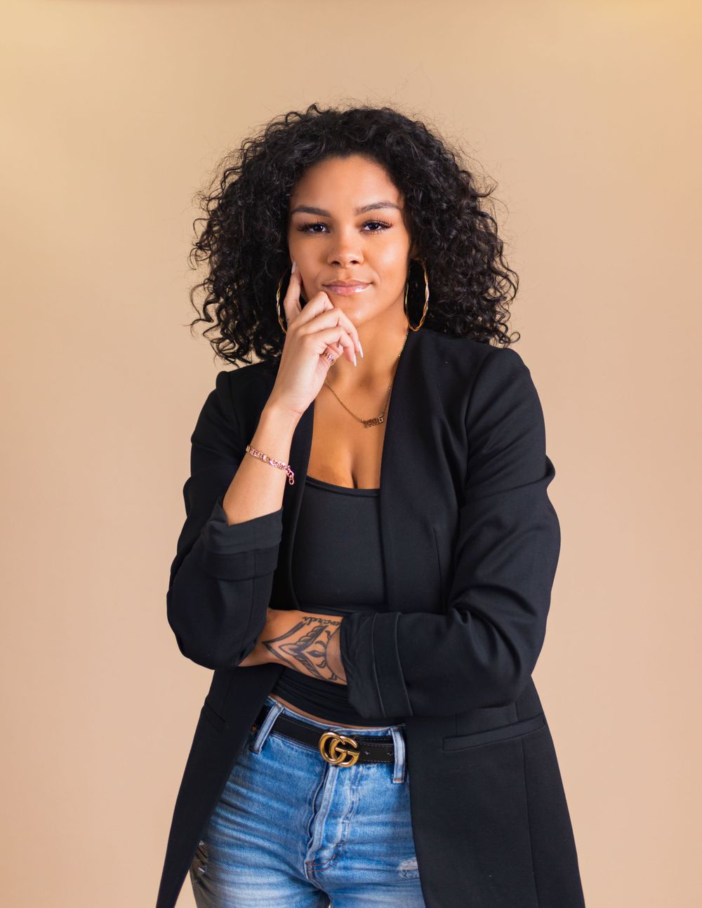 Stylish portrait against beige background featuring black blazer, crop top and designer belt.