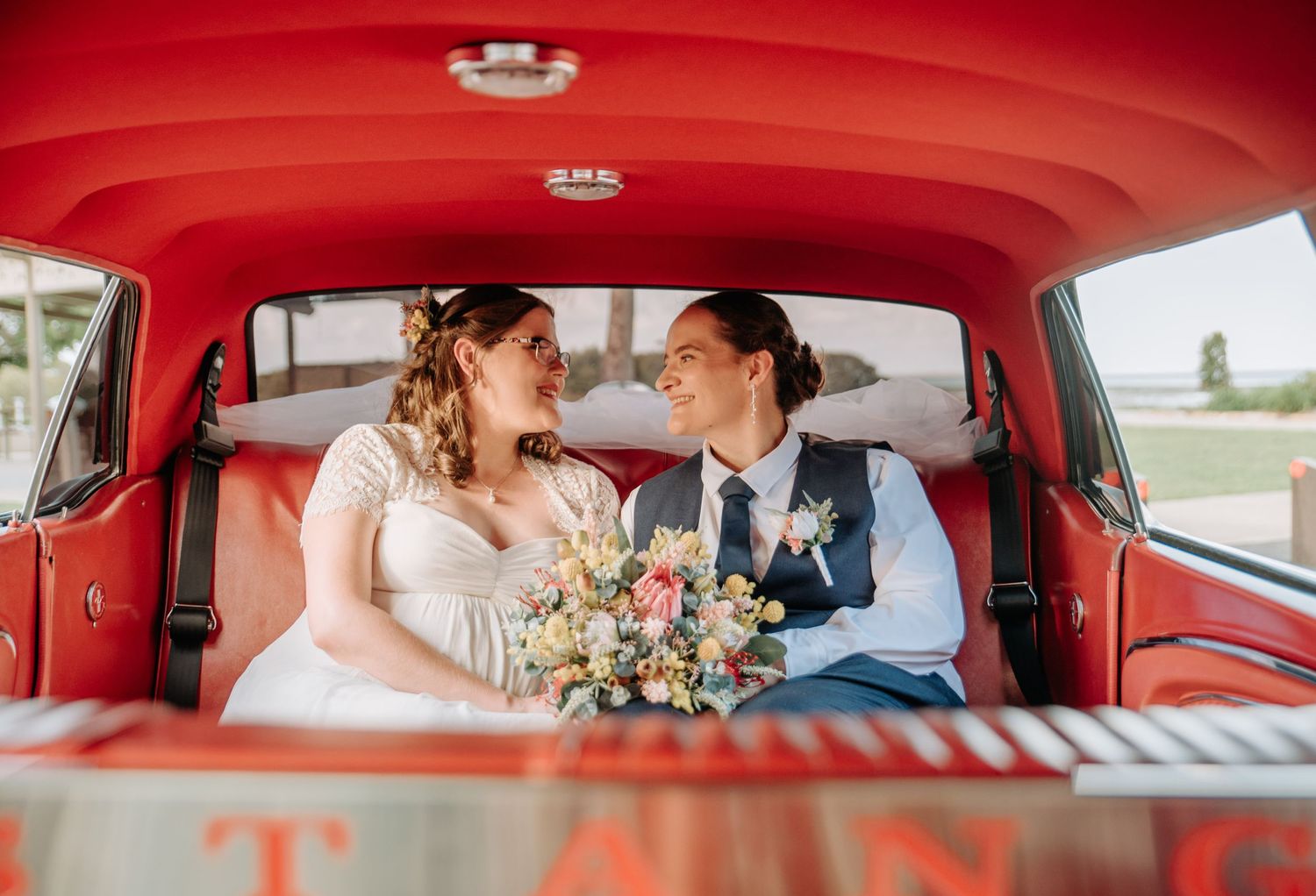 A candid moment inside a vintage car with red interior during a wedding celebration.