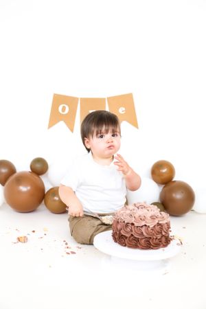 Baby celebrates first birthday with chocolate cake and brown balloon decorations.