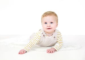 Baby in striped onesie lays on white blanket during photography session.