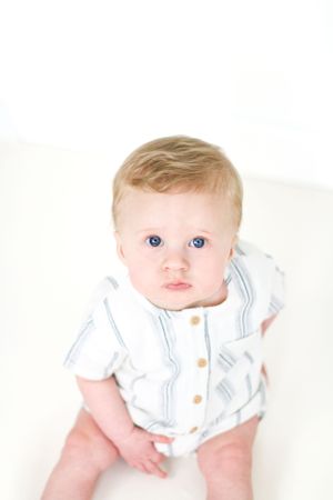 A baby wearing a white button-up romper poses against a light background.